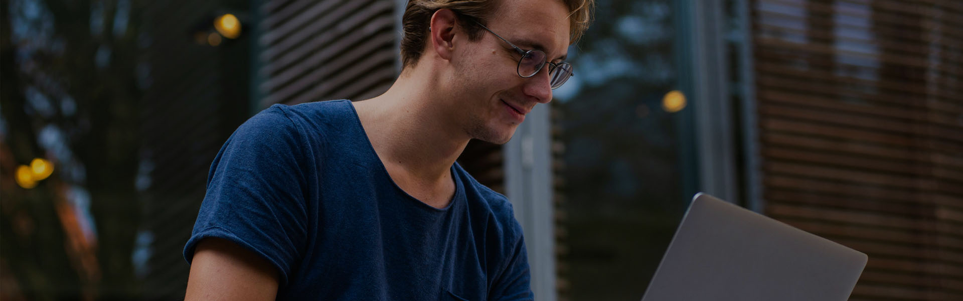 Homem de camisa azul no quintal olhando para o notebook e sorrindo