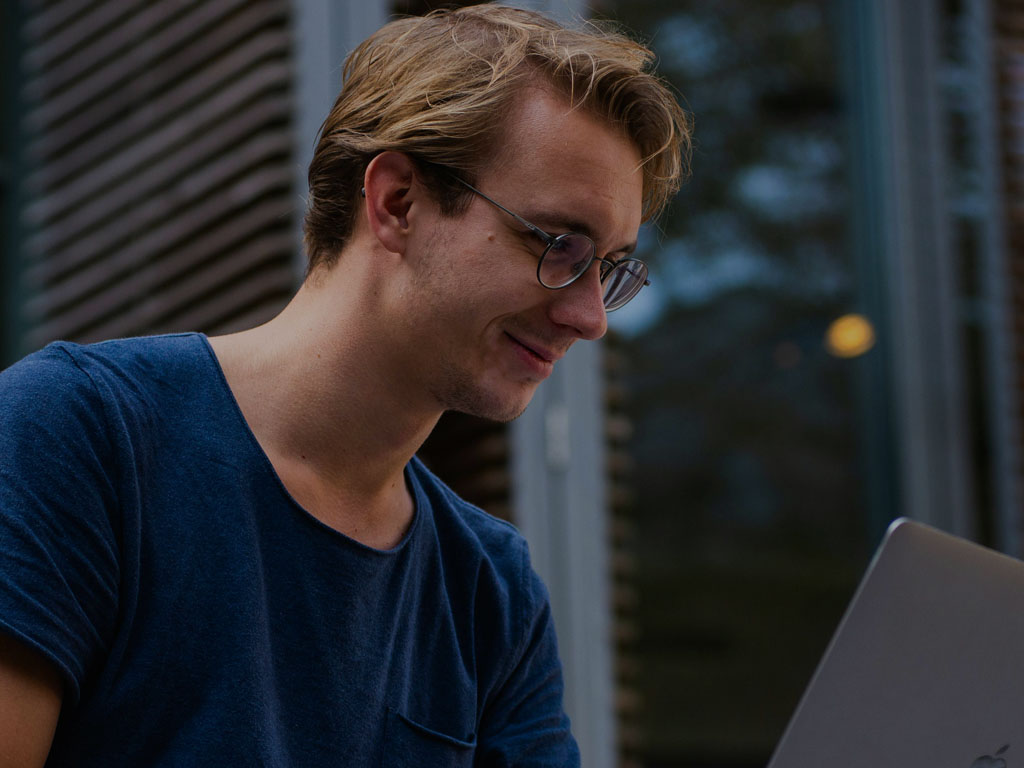 Homem de camisa azul no quintal olhando para o notebook e sorrindo